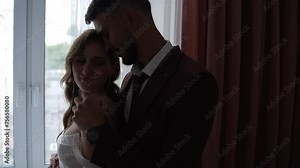 Happy bride and groom in formal wear standing next to each other by a window