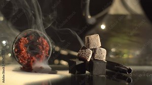 Dark composition of the hookah embers and equipment for smoking placed on the table is wrapped with thick cloud of smoke.