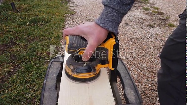 Hands of a carpenter working with cordless orbital palm sander sanding a wooden plank