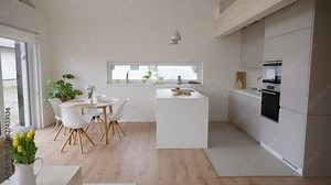 Minimalistic kitchen with gray furniture, cabinets and countertop, kitchen island and build-in appliances. Round dining table on wooden floor.