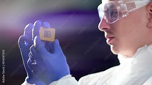 A young computer engineer holds and tests a processor. Close-up of a male engineer holding a microchip with gloves and examining it - a state-of-the-art electronics manufacturing plant Stock Video