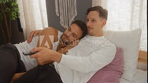 Men cuddling in bedroom watching tv on bed showing their close bond in a relaxed home setting