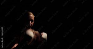 Close-up side view footage of a determined blonde female boxer aggressively striking blows on a boxing bag during training.