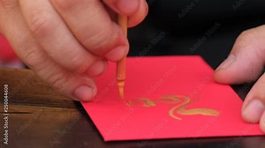 Vietnamese scholar writing calligraphy on red envelope, ang pao in lunar new year. Calligraphy festival is a popular tradition during Vietnam Tet holiday. Calligrapher draw handwriting in springtime