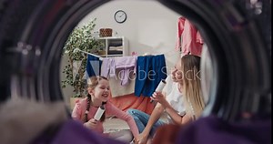View from inside the washing machine drum into the laundry room. Mother and daughter are having a great time, singing to the clothes rollers, fooling around.