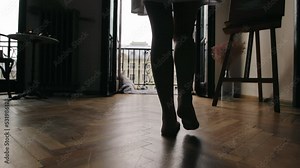 Silhouette of female legs slowly walking towards the window. Women's legs go to the balcony, where the houses of the city can be seen in the background.
