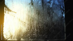 Drops of rain flow down the glass. Sun through the wet window. Foggy window, close-up. The window is melting. Morning sun in a rainy window. Spring warming.