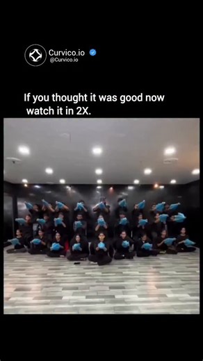 Curvico Explained on Instagram: "This mesmerizing visual isn't just a dance routine - it's a carefully engineered form of synchronized visual art where movement, geometry, and coordination blend to create a single living structure. What you're seeing is a group of performers using identical blue props, likely umbrellas or hand fans, arranged in precise layers to form patterns that appear almost computer-generated when viewed from the front. This technique, often used in large- scale stage produc