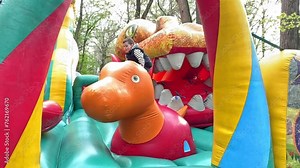 Child jumping on colorful playground trampoline. Kids jump in inflatable bounce castle on kindergarten birthday party Activity and play center for young child. Little boy playing outdoors in summer.