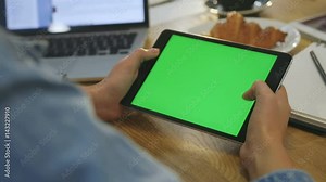 Woman hands using digital tablet touchscreen device with green screen in cafe. Woman scrolling photos, news, pages on tablet computer. Close-up. Chroma key