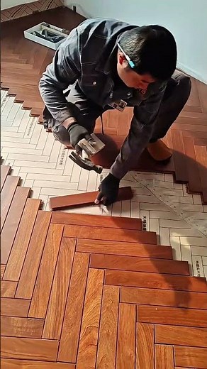 A worker installs wood flooring in a herringbone pattern and taps the pieces into place carefully