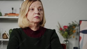 Blind woman reading braille book using fingers, sitting in living room, poorly seeing female person learning to read, home education for people with disabilities, touching letters on sheet of paper.
