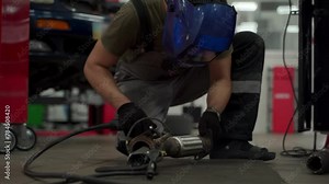 Auto mechanic welds car exhaust flex pipe using welding equipment in garage, performs catalyst repair under vehicle. Professional works on auto exhaust system servicing, fixes broken parts.