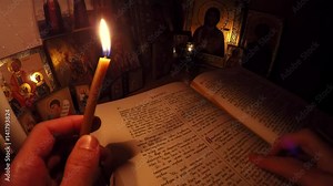 Monk reads the Bible and prays before the icons with candles