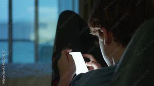 A rear view of a teenage boy using his smartphone by the window. Shot from back