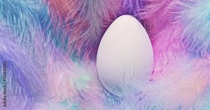 Soft fluffy pastel feathers blowing in the wind with a single white Easter Egg. Gentle Easter theme with egg in delicate nest of feathers.