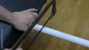 A man's hand using a tool hacksaw cuts off the PVC pipe.
