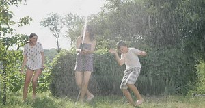 Mother and children play with water from a garden hose. A happy family rests, rejoices and splashes with water in hot summer weather. Watering in the garden near the house.