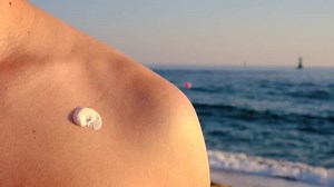 Man applies sunscreen to his body against the backdrop of the sea close-up.