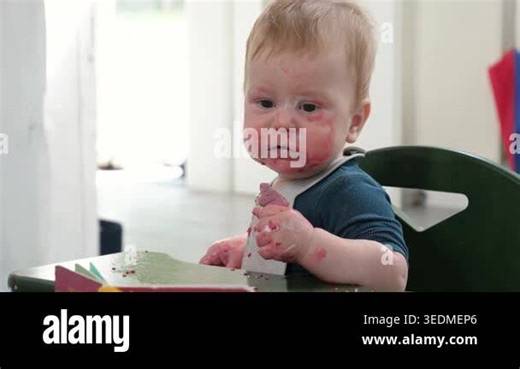 Messy Infant indulges in sweet treat during mealtime. Curious baby eating cookie at home in high chair Stock Video Footage - Alamy
