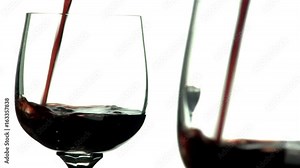 Macro of red wine being poured into wine glass with mirror reflection creating double image. Shot with angled mirror and white background and focus on rear mirror image