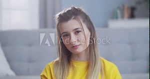 Close up front portrait of beautiful confident cute smart blonde looking at the camera and smiling. The woman confidently looks forward with a satisfied expression on her face at stylish living room.