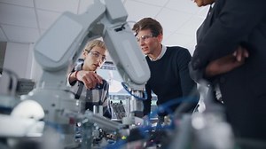 Two Concentrated Students Express their Ideas and Assumptions Standing Around Bionic Robot Arm with Female Teacher at University Class. Computer Science Education Build, Learn Concept. Low Angle View