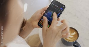 Freelancers in coffee shops multitask, working on their projects while keeping an eye on the stock market using their smartphones