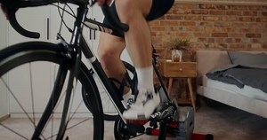 Young focused man rides a bike simulator in a modern home interior. Cycling indoor, cardio workout