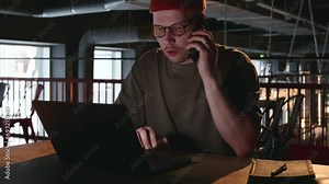A male hacker or Internet fraudster communicates on the phone with a person he is trying to deceive and simultaneously enters data on a laptop. High quality 4k footage