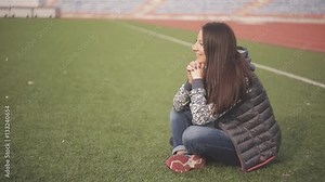 Beautiful young woman on the football field. Girl sitting on the green grass on the playground