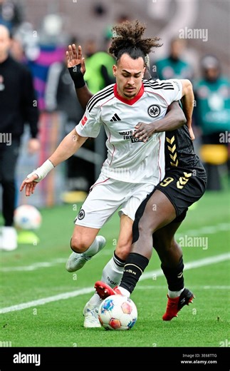 05 April 2026, Hesse, Frankfurt/Main: Soccer, Men, Bundesliga, Eintracht Frankfurt - 1. FC Köln, Matchday 28, Deutsche Bank Park, Ragnar Ache (r, 1. FC Köln) and Arthur Theate (Eintracht Frankfurt) fight for the ball. Photo: Uwe Anspach/dpa - IMPORTANT NOTE: In accordance with the regulations of the DFL German Football League and the DFB German Football Association, it is prohibited to utilize or have utilized photographs taken in the stadium and/or of the match in the form of sequential images 