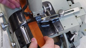 Operator is adjusting automatic leather skiving machine in a haberdashery manufactory. Splitting, aligning and cutting edge of leather details, electrical motor-driven machine.