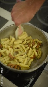 unrecognizable young chef tossing pasta with tomato sauce in pan in slow motion while cooking in restaurant kitchen. vertical video for tik tok or reels Stock Video