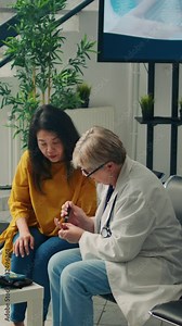 Vertical video: Senior doctor measuring sugar level with blood sample to do insulin test with glucometer for asian patient with diabetes. Checking glucose at medical checkup examination at clinic.