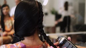Female stylist applying hairspray fixing plaiting hairstyle on brunette hair back view slow motion. Hairdresser finishing hairdo making final touch with spray. Overview