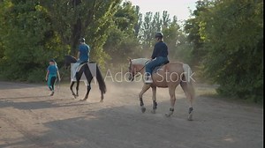 Back view of man and woman riding horses together. Couple learning to ride horse. Male equestrian with instructor walking on horse racetrack.