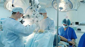 Team of surgeons conducting a precise operation with the assistance of an electron microscope in a sterile operating room. Advanced medical technology used for intricate procedures.