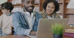 African American students using laptop looking at screen and talking studying in university library together. Modern technology and academic education concept.