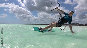 SLOW MOTION, CLOSE UP: Happy young woman kiteboarding in Tanzania drags her hand along the surface of crystal clear ocean. Fit female kiteboarder surfs around the blue lagoon in stunning Zanzibar.