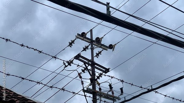 A power pole with electrical wires against a cloudy sky backdrop.