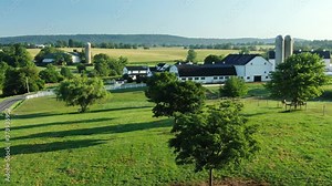 Amish family farm in Lancaster County Pennsylvania, slowly rising aerial reveals pristine black and white farm barn buildings and green meadow during summer magic hour light