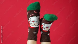 Women's feet in Christmas socks with Santa Claus on red background, legs up dancing