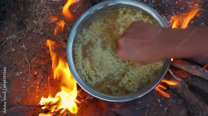 Directly above shot of noodles being cooked on a campfire in forest, girl hand stirring noodles. Cooking food at fire in wild. Party in camping, Summer Camp Travel activity for relaxing.