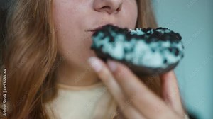 Close up portrait of a hungry 30s woman eating donut with white frosting. Eating donut when takeout and delivery. Fast food takeaway back home. High quality FullHD footage. High quality FullHD footage