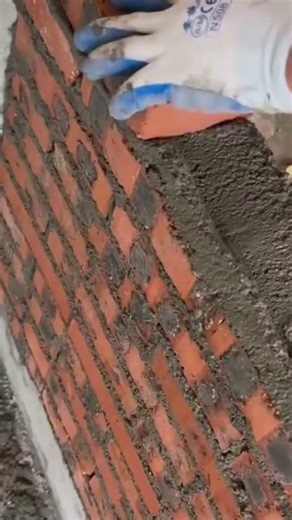 applying a thick layer of white plaster onto a textured grey wall surface using a square metal hand