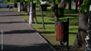 4k video. Public garbage trash container made of wood with a black plastic bag inside on the streets of a city in summer landscape. Keep the cities clean.