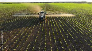 Aerial video of tractor spraying soil and young crop in springtime in field. Tractor spraying pesticides on soy field with sprayer at spring. Nozzle of the machine industry sprinklers sprayed.