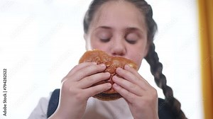 schoolgirl child eating hamburger breakfast at recess. training nutrition lifestyle for schoolchildren fast food concept. schoolgirl child eating breakfast sandwich from a paper bag with a backpack