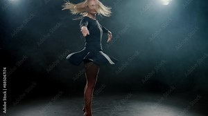 Graceful blonde woman in black dress dancing alone in dark studio, slow motion. Beautiful lady performing contemporary choreography on stage, rehearsing in dance hall, bright soffit and artistic smoke